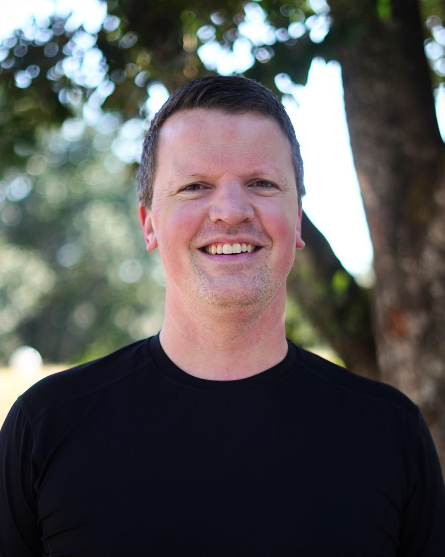 Nate Dame, smiling, outdoors under a tree.